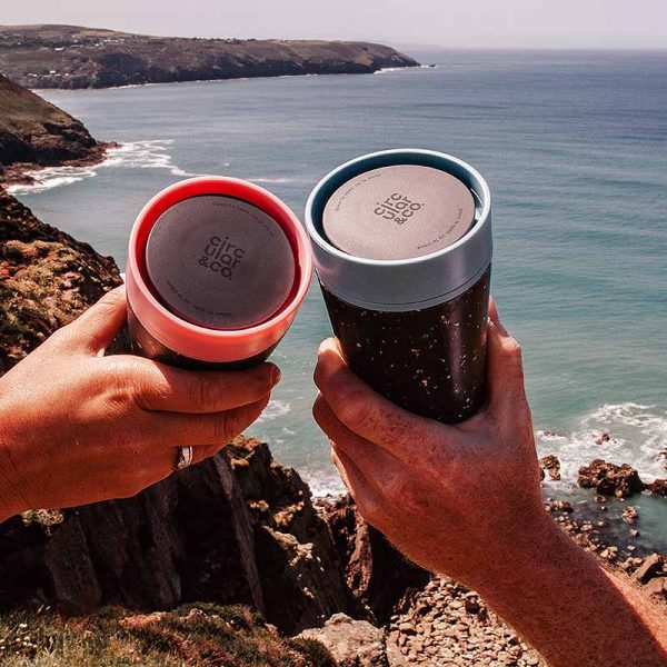 two hands holding cups overlooking sea and cliffs