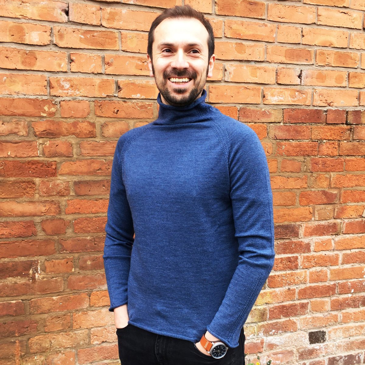 man wearing jumper in front of brick wall