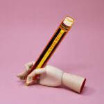 wooden hand holding pencil on pink background