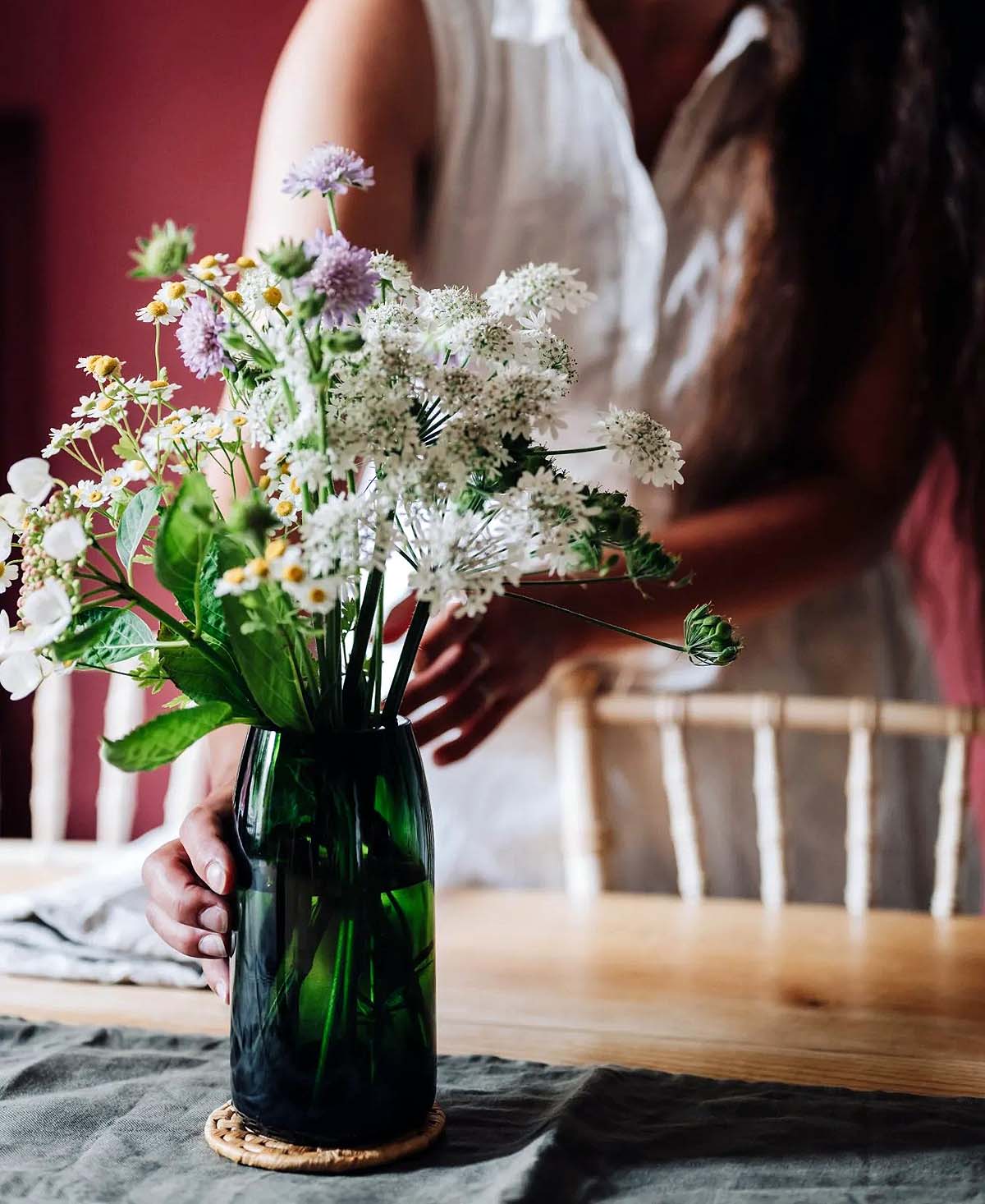 forest-green-glass-vase vase with flowers being placed on a cloth on a table