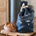 full bread bag standing next to a loaf of bread on a bread board next to a bread knife on a work top