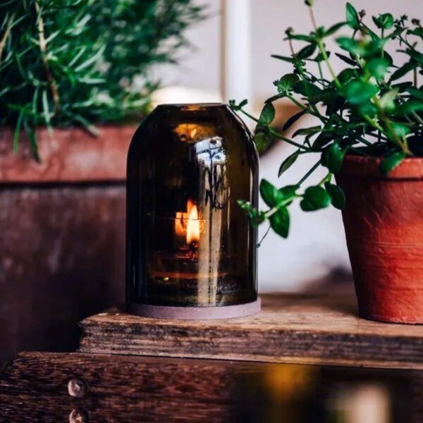 glass dome containing lit tea light on small table next to plants