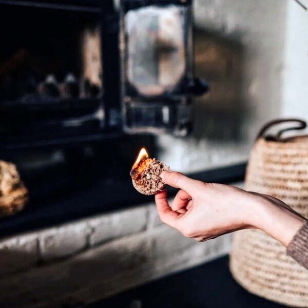 hand holding lit firelighter in front of a wood burner