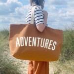 woman standing on sand dunes holding bag