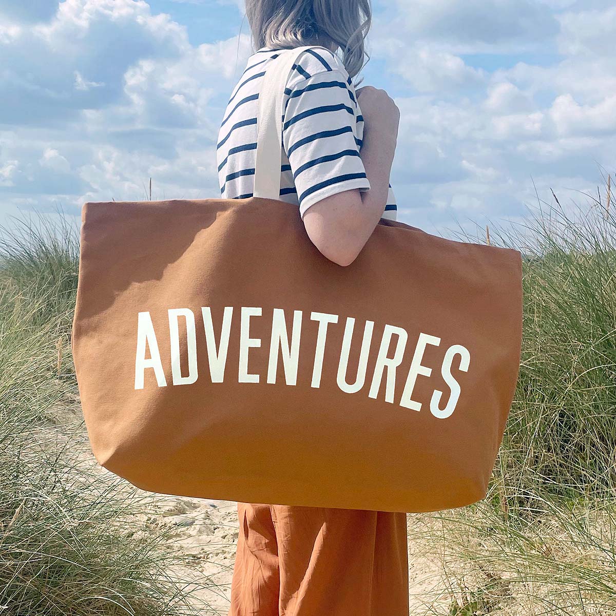 tan-really-big-adventures-bag woman standing on sand dunes holding bag