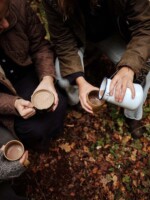 view of hands sharing hot chocolate from a flask in an autumn wood