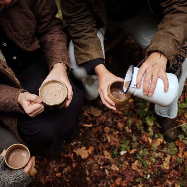 view of hands sharing hot chocolate from a flask in an autumn wood