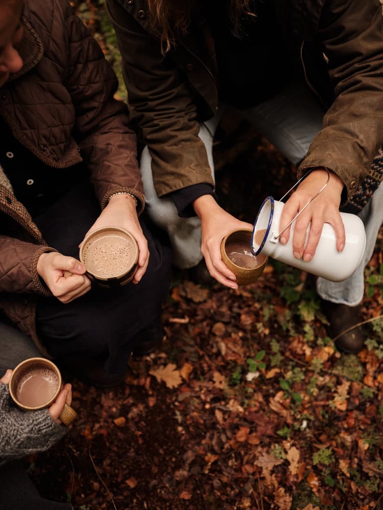 clothed hands in an autumn wood holding cups with hot chocolate